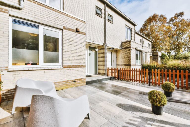 Modern pale brick townhouses with a paved terrace and a wooden picket fence