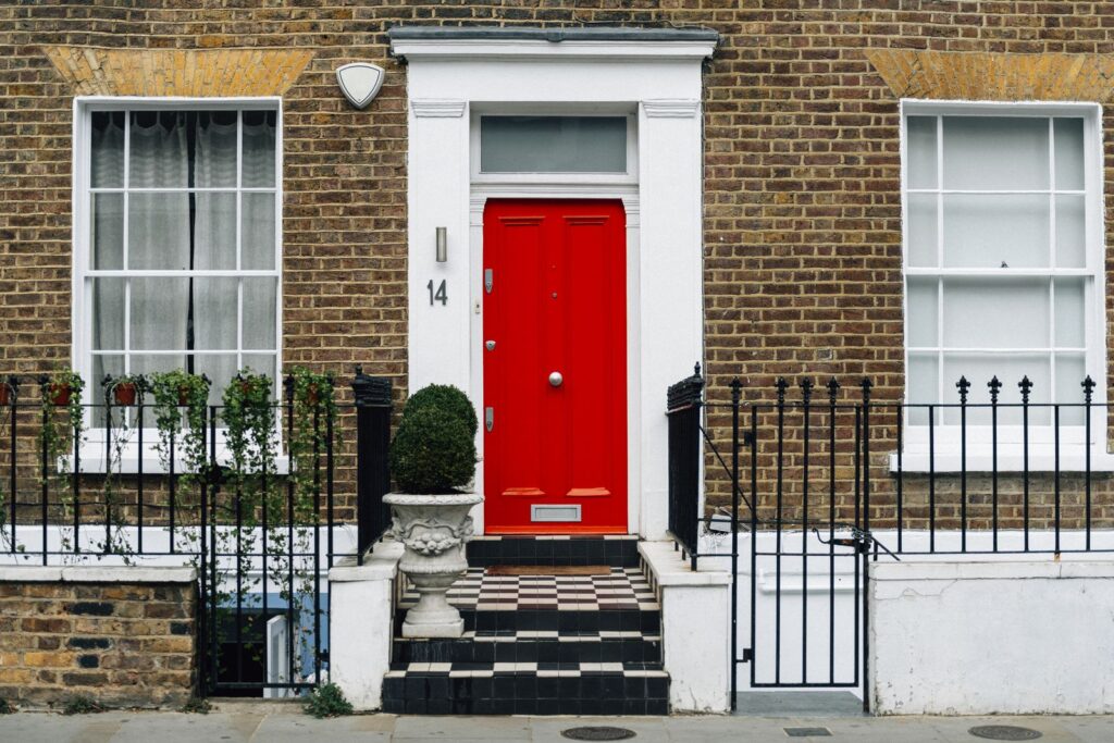 Red front door in a brick building with steps and railings